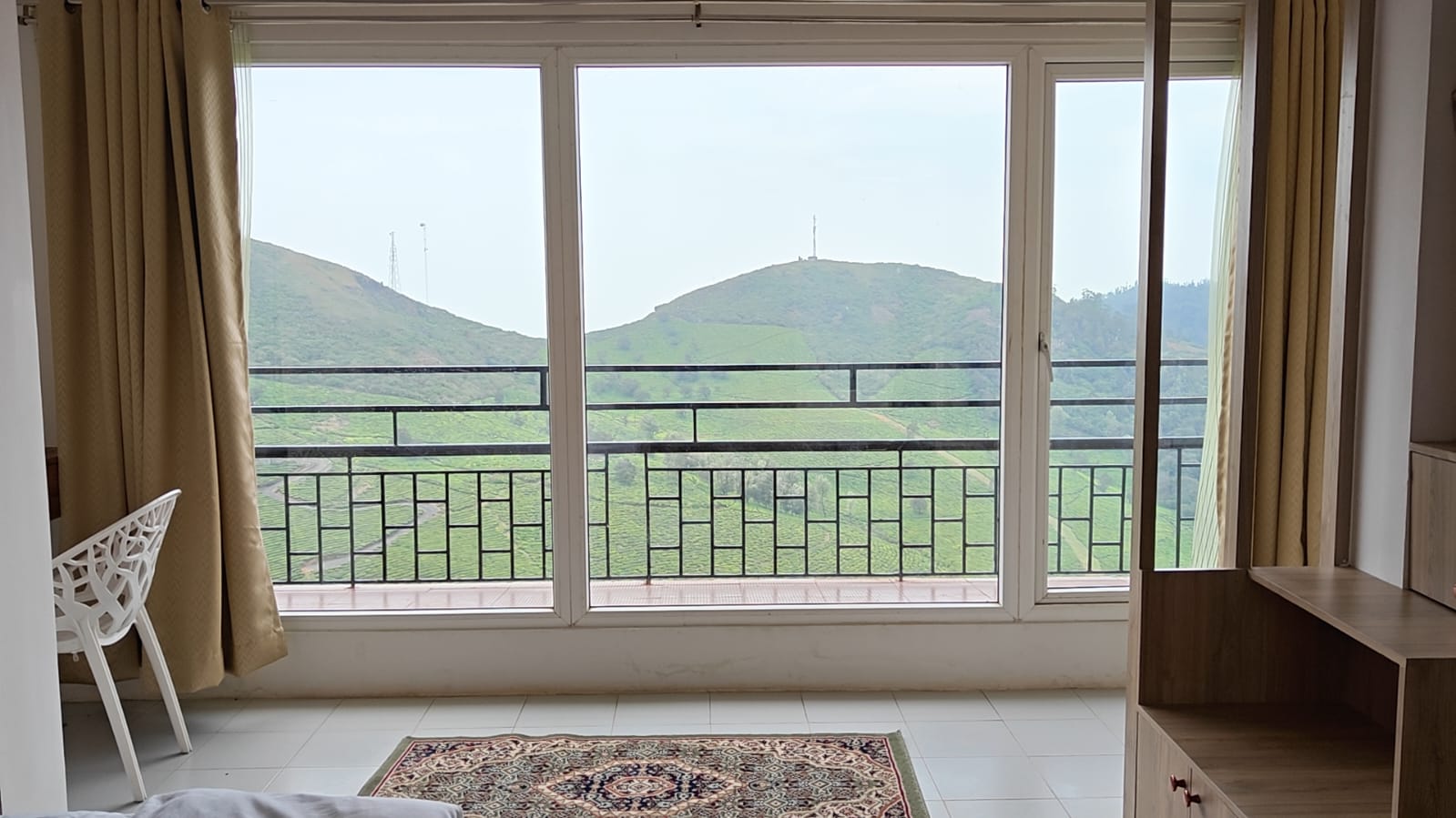 A bedroom's full-width windows opening onto a balcony, tea gardens climbing the hill beyond