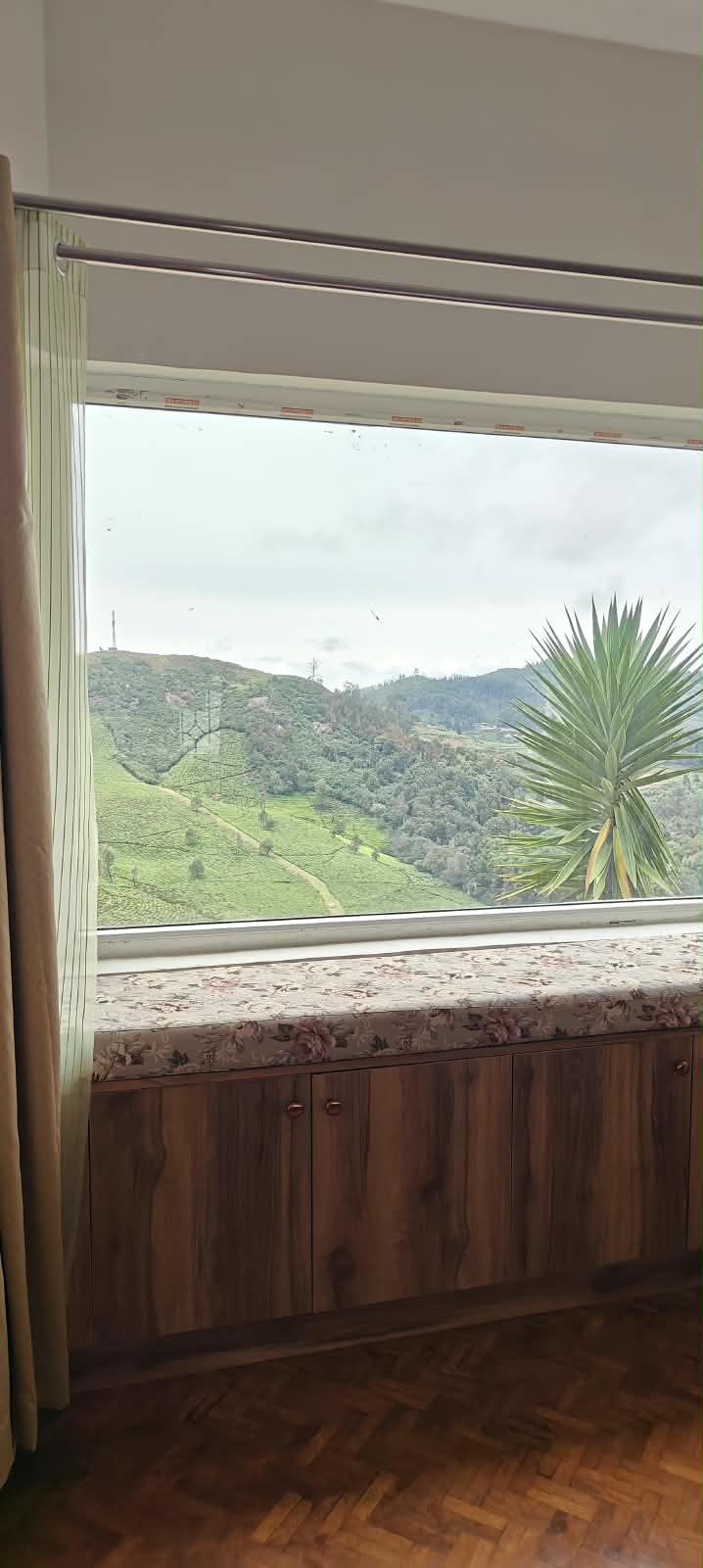 A four-poster bed beside a bay window with a cushioned seat, looking out over the green hillside