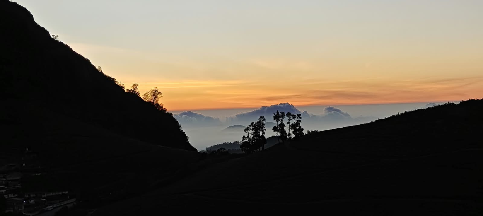 The sun rising behind the hills, warm light spreading over the valley and the village below