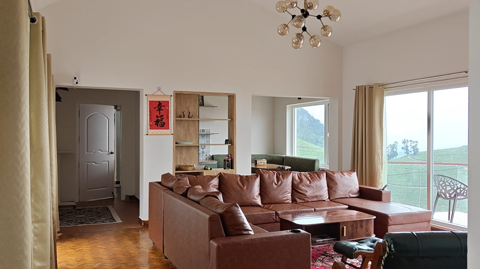 The living room with its leather sectional and brass chandelier, the dining nook and open shelves beyond